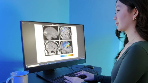 Molly Zhao at her computer, displaying magnetoencephalography (MEG) brain scans on the monitor.
