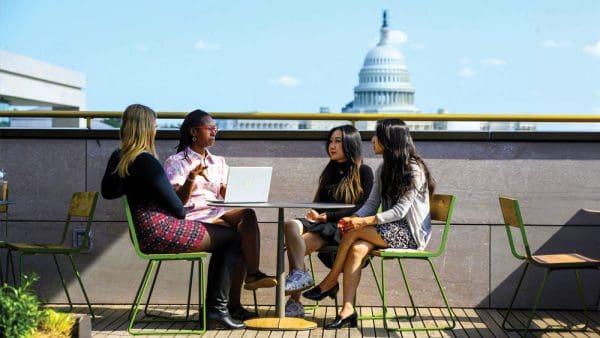 students in discussion at outdoor table at the Hopkins Bloomberg Center, U.S. Capitol in view in the background