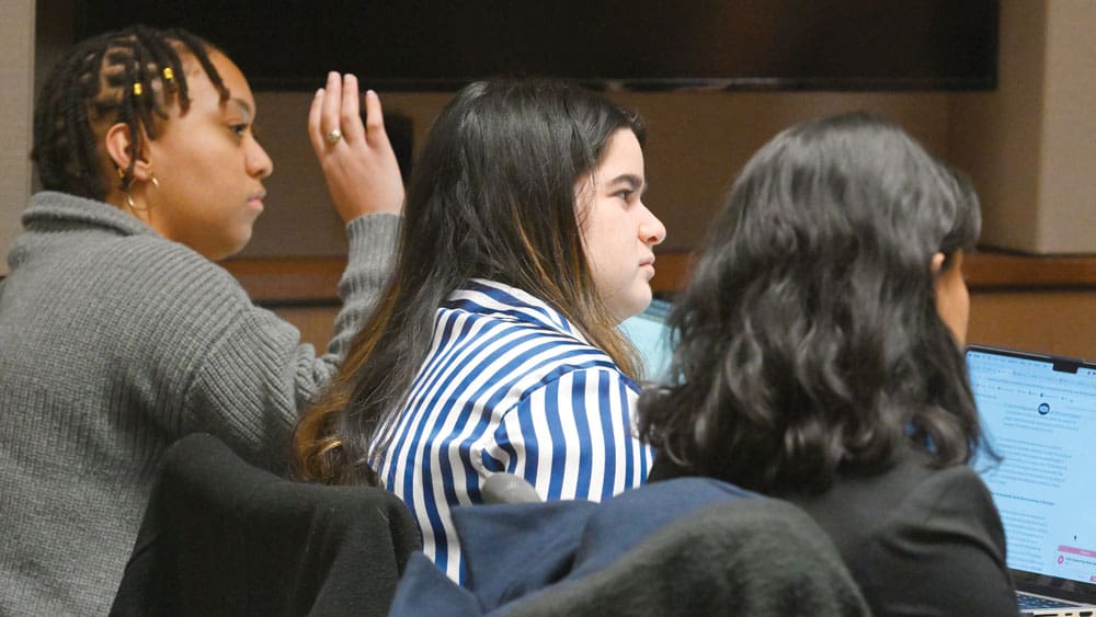 side view of three students - one raising hand