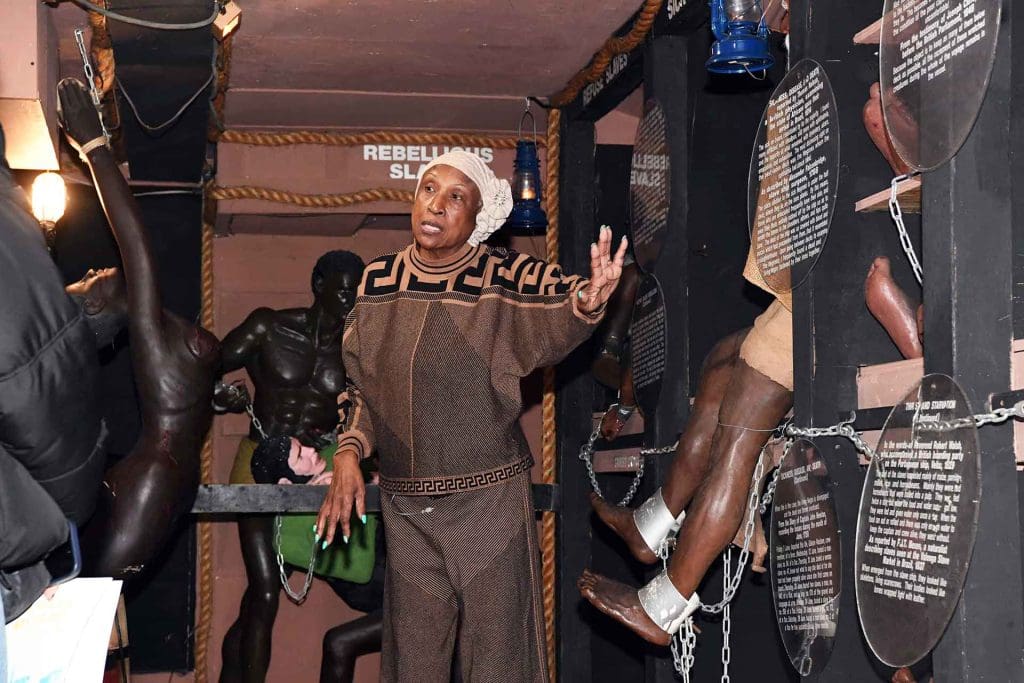 a woman in a head wrap standing in front of a Blacks in Wax Museum exhibit