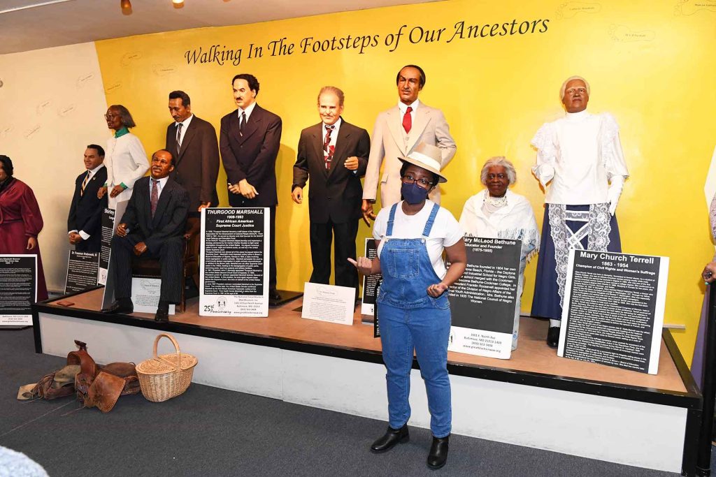 a woman standing in front of multiple statues of famous Black politicians and businessmen