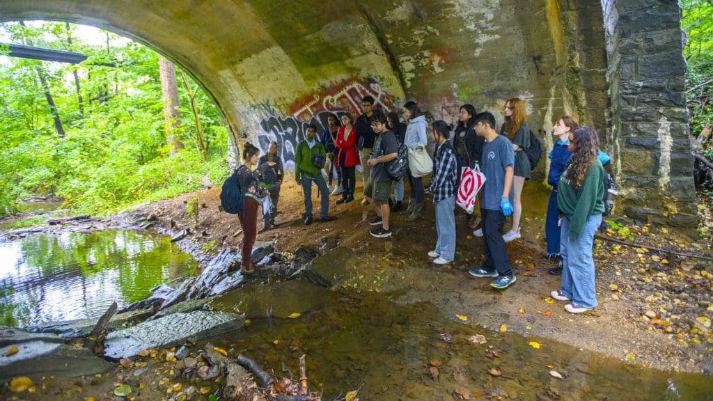 Pandian's class gathered by creek bed under bridge listening to guest speak