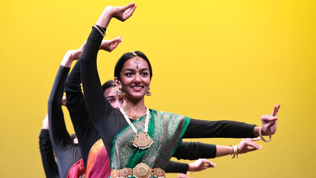 Three people in decorative dress with arms outstretched in a Bhangra pose