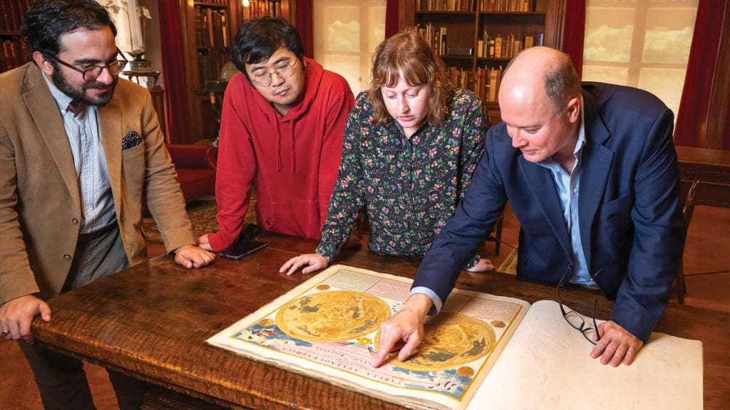 Earle Havens with three Fox Stern Fellows looking at book in Evergreen Library.