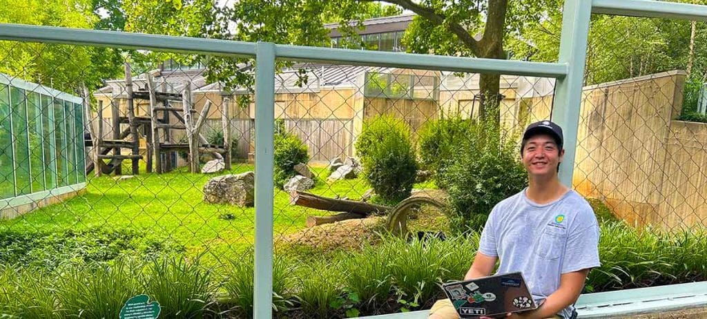 Alex Jeffords sits in front of a zoo enclosure