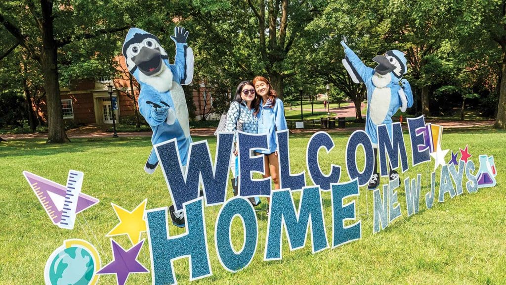 parent and student smiling in front of "Welcome Home New Jays" sign