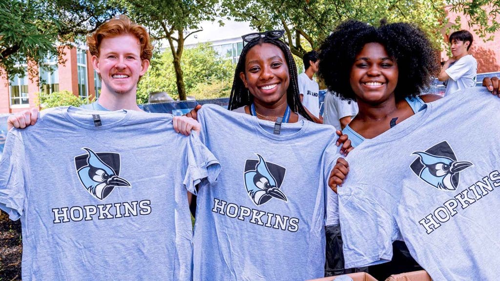 three smiling students holding up Hopkins t-shirts