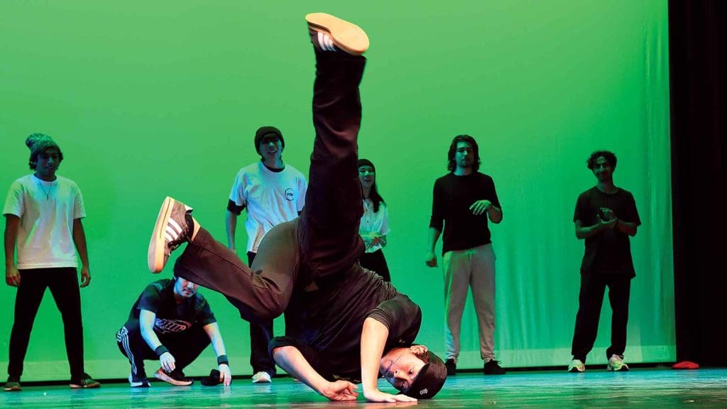 student breakdancing on Shriver Hall stage as others in the dance group look on