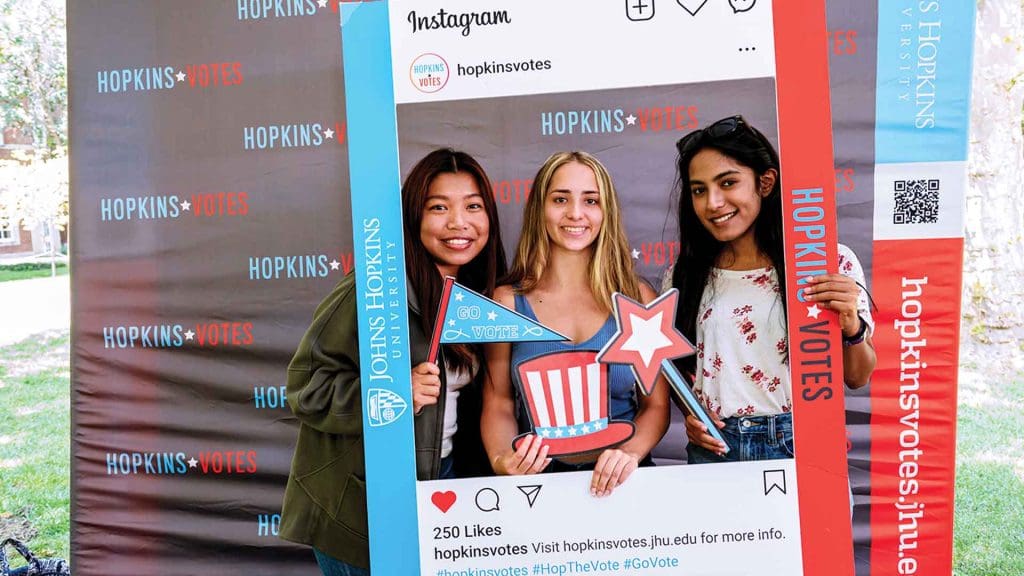 three smiling students holding an Instagram "Hopkins Votes" frame