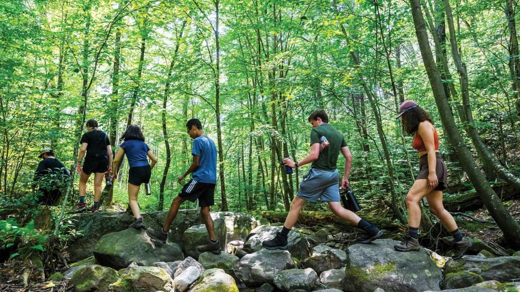 students hiking over rocks through woods