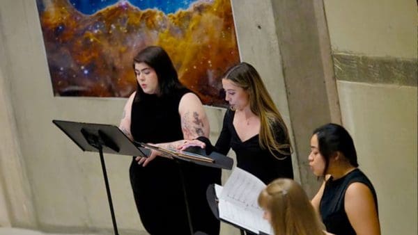 three singers with music stands in front of an image from the Webb telescope
