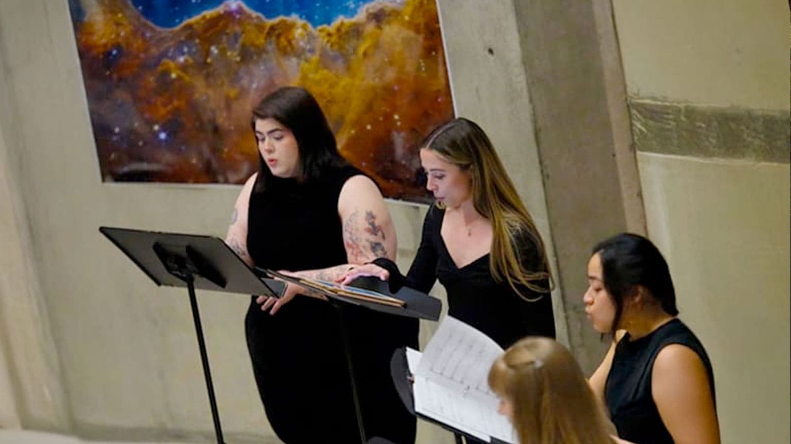 three singers with music stands in front of an image from the Webb telescope