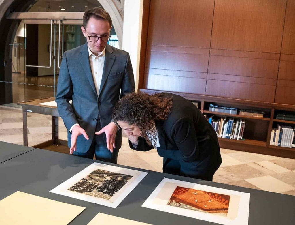 Jason Mientkiewicz ’25 PhD with Leslie Cozzi, curator and head of the Baltimore Museum of Art’s Department of Prints, Drawings, and Photographs, at a table looking at two lithograph prints.