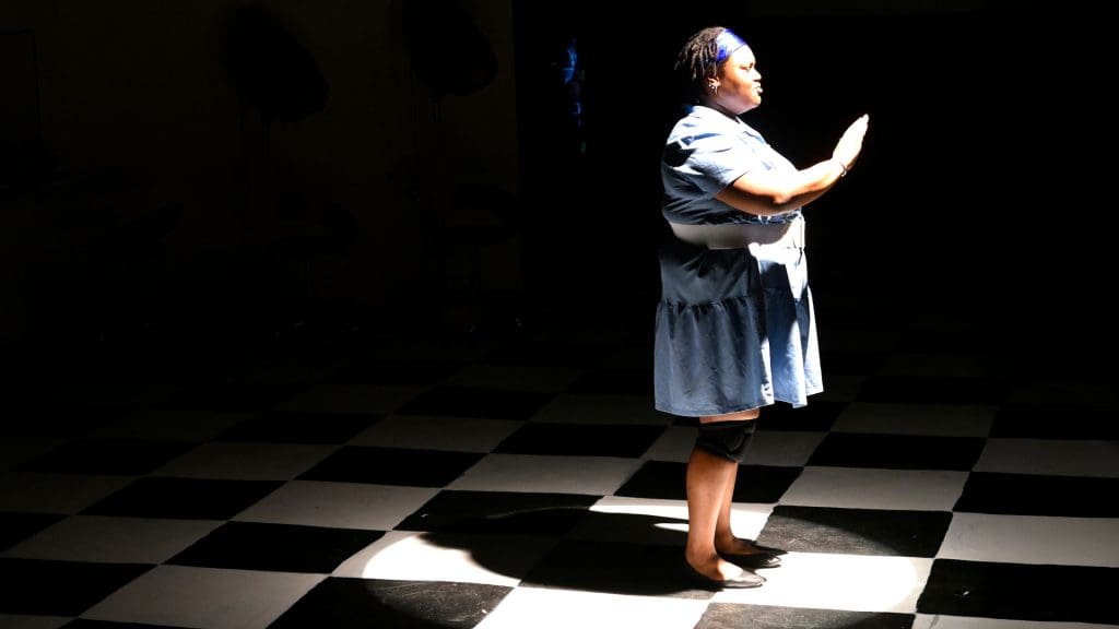 a woman standing alone on a tiled floor with darkness behind her