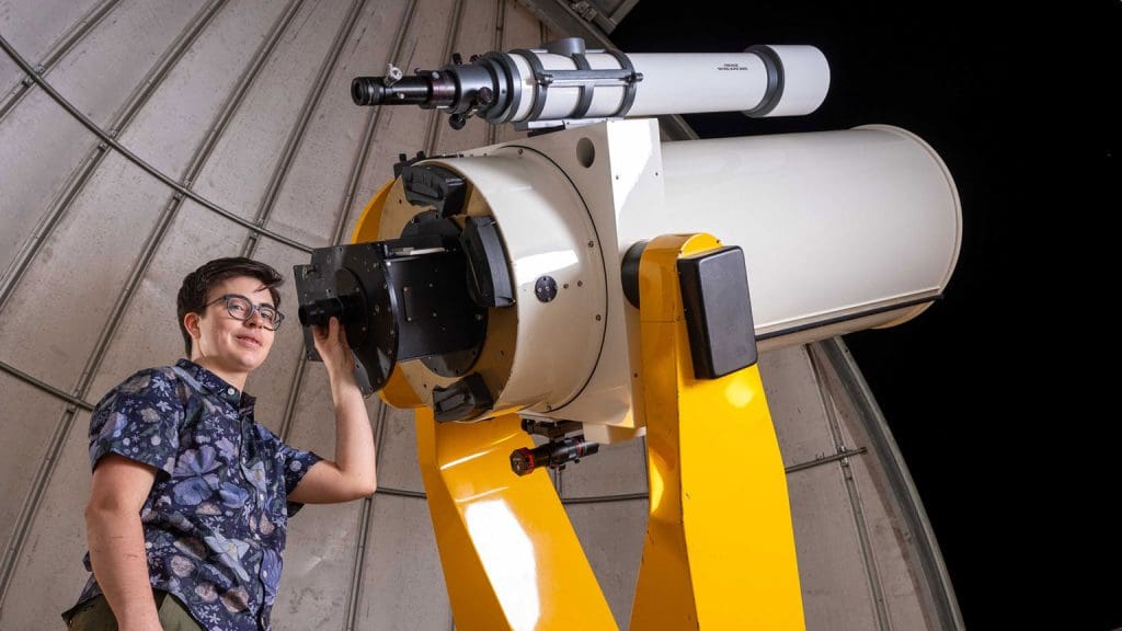 Ezra Sukay next to telescope inside the observatory on Homewood Campus.