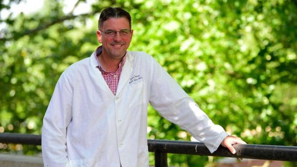 Dana Ferraris standing in front of bright green trees.