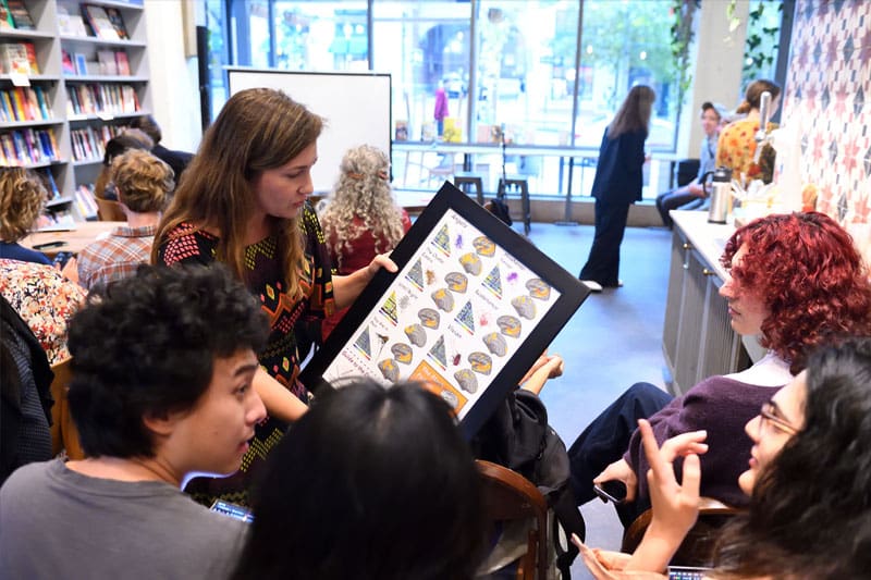 Dora Malech holding the framed Flash Fiction poster, showing it to a crowd that is gathered.