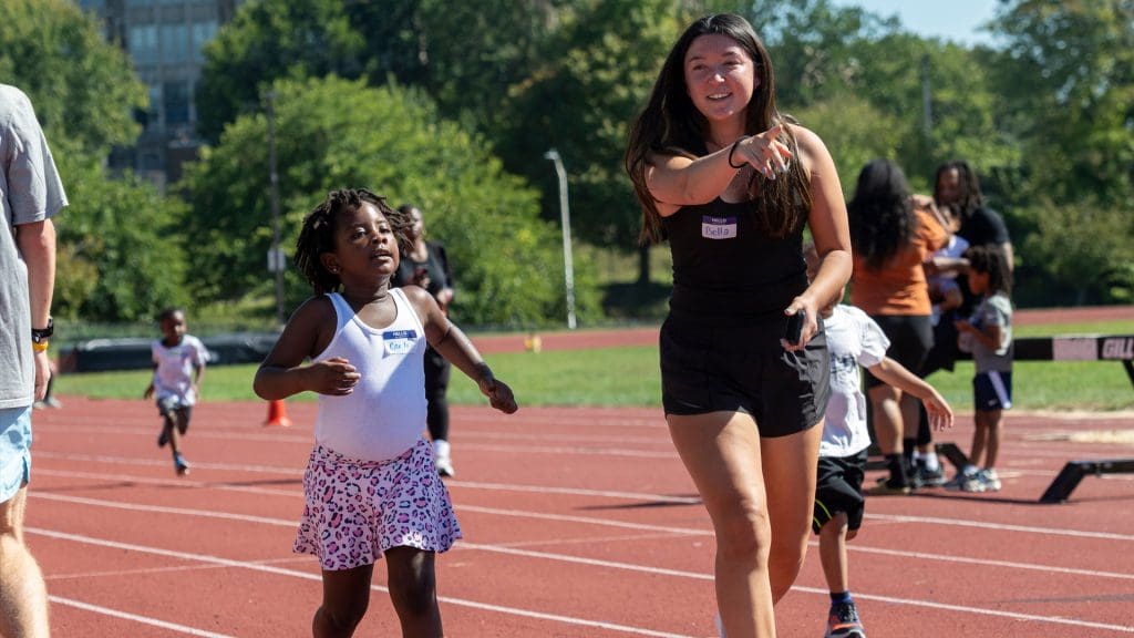 JHU Volunteer running with children on the track at the Run Baltimore event.