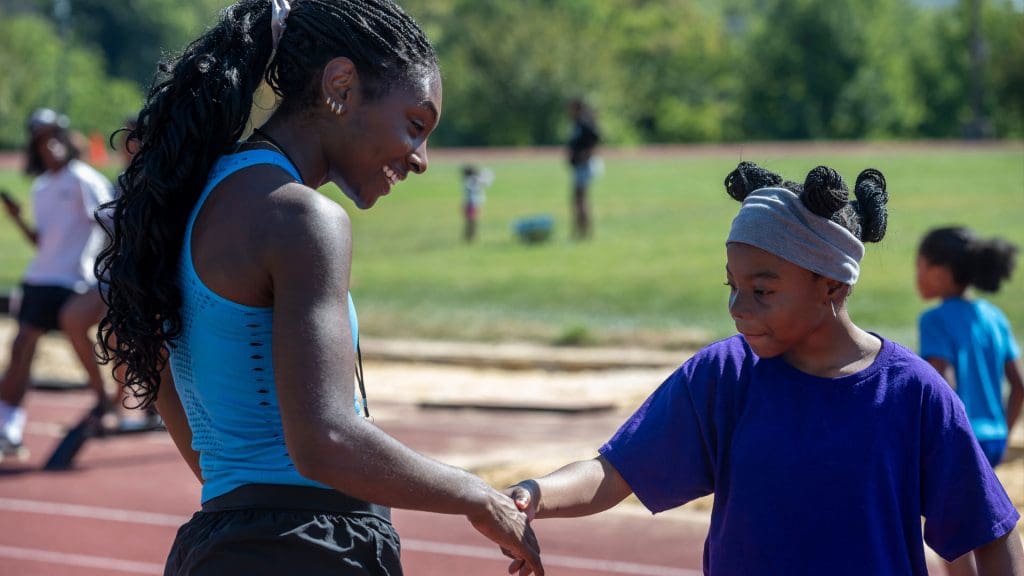 A JHU Volunteer shaking hands with one of the kids at the Run Baltimore event.