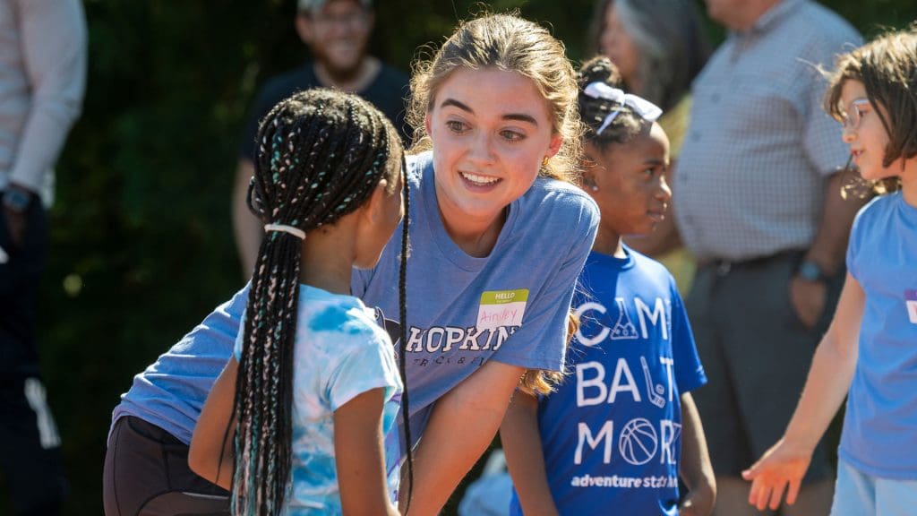 JHU Volunteer leaning down to speak to a child at the Run Baltimore event.
