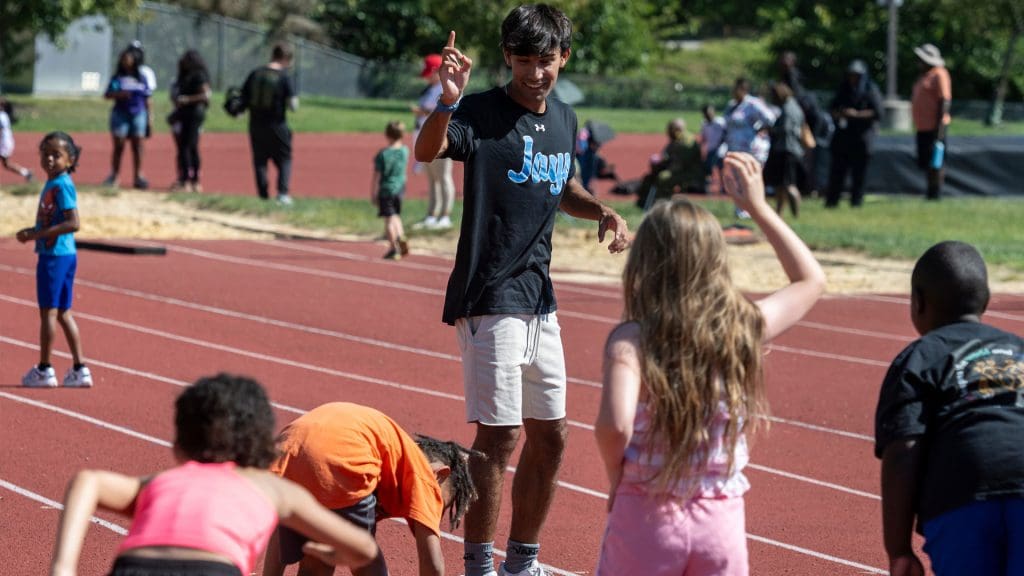 JHU Volunteer leading children in activity on the track at the Run Baltimore Event.