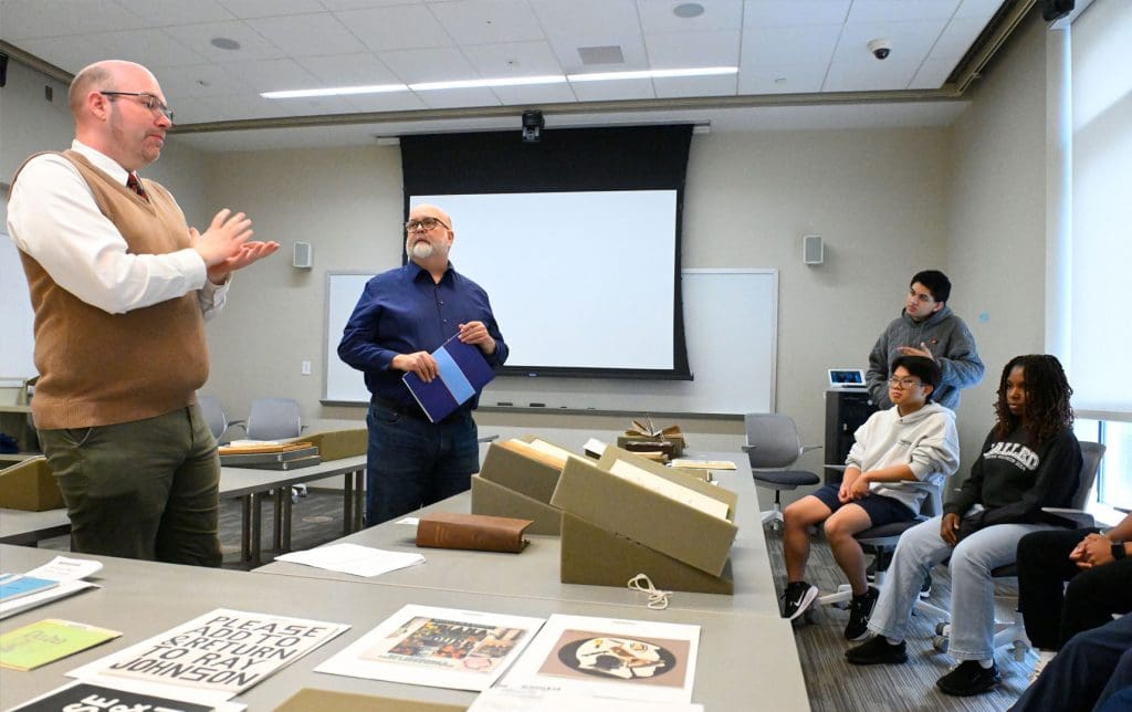 Richard Essam (left) and librarian Donald Juedes look through unusual archival documents with “Playing with Words” students.