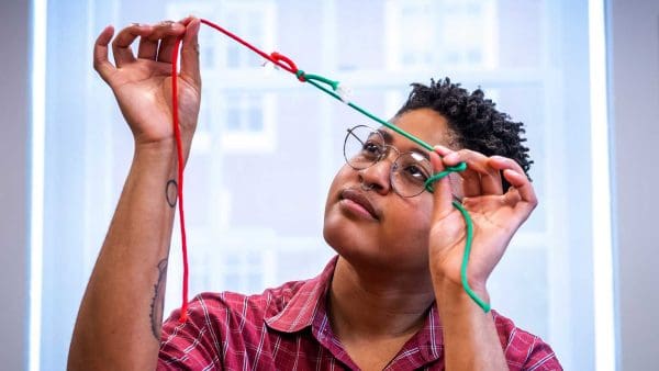 Sholei Croom looking at an example of a tied knot with contrasting red and green string.