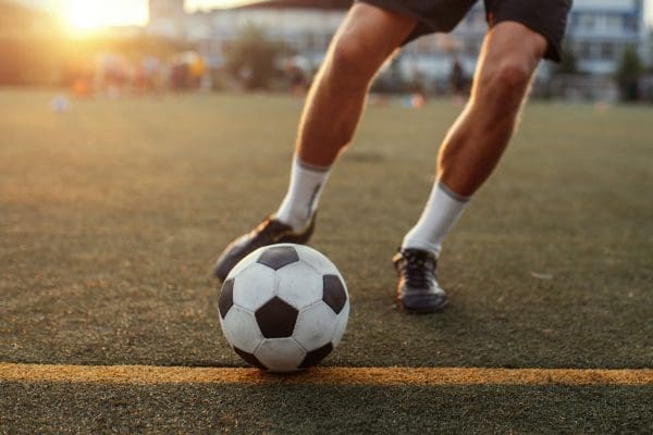 Persons playing soccer, image is focused on the legs and soccer ball.
