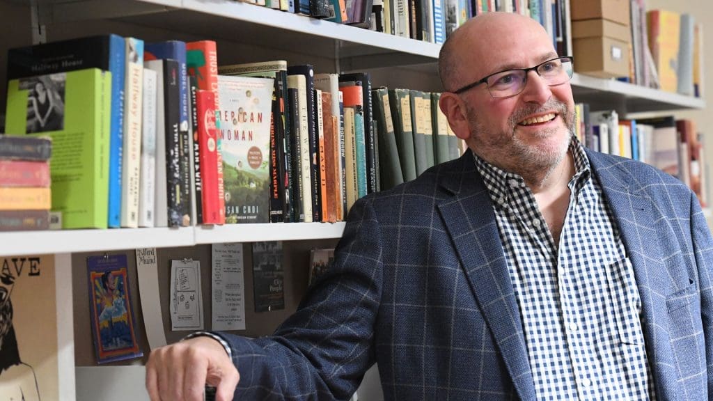 Gwydion Suilebahn next to a book shelf.