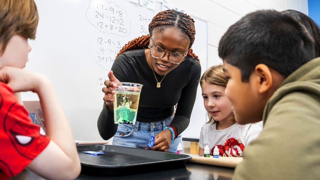 Medfield students watching a Johns Hopkins student demo hands-on science with food coloring and oil in a cup.