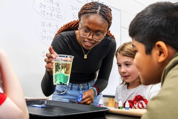 Medfield students watching a Johns Hopkins student demo hands-on science with food coloring and oil in a cup.
