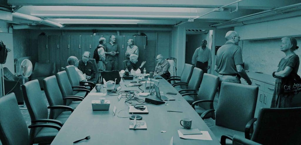 Large table, mostly empty, surrounded by small groups of 2-3 Academy faculty in conversation. One person is walking into the room.